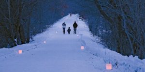 Family with young child walking a winter trail with candlelight.